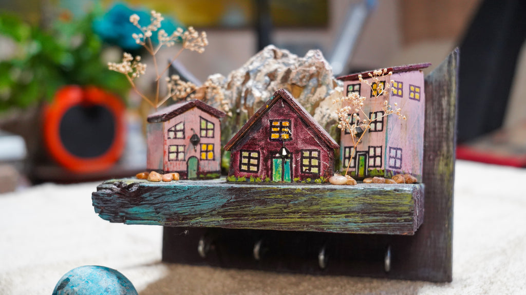 Manualidad de tres casitas de colores rosados con arboles y montaña para sujetar llaves